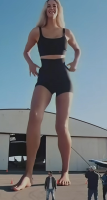 giantesshug gentle giantess blonde long_hair clothed barefoot smiling bodysuit standing size_comparison hangar cameramen ai_art