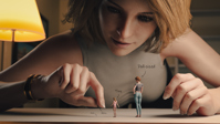 breasts micro butt handheld barefoot jeans brunette shorts table shrunken_woman dangle indoors bending_down bracelet lamp pinched looking_at_tiny digital_render mshrinker hair_bun multiple_sizes