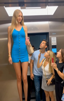 enhanced_art blonde long_hair clothed dress mini_giantess standing onlookers size_comparison cellphone elevator ai_art mulitple_people